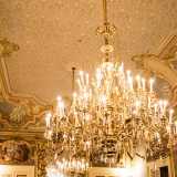 ...e dai due lampadari di cristallo. Questi ultimi pendono da un soffitto con motivo a intreccio e putti che sorreggono vari stemmi