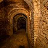 Da una scala in legno risaliamo qualche gradino per accedere a un lungo corridoio, forse un camminamento difensivo del vecchio fortilizio, suddiviso da una serie di spettacolari archi divisi da volte in pietra perfettamente lineari tra di loro
