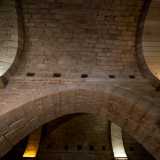Qui su due file di possenti pilastri poggiano alti archi in pietra che reggono le volte a botte realizzate con conci locali, dividendo la sala in tre corridoi