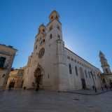 Qui incontriamo la facciata in pietra bianca dell�edificio, chiusa dalle due torri campanarie in stile romanico che sovrastano un magnifico rosone e un portale decorato