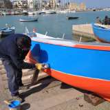 Un pescatore mentre dipinge la sua barca 