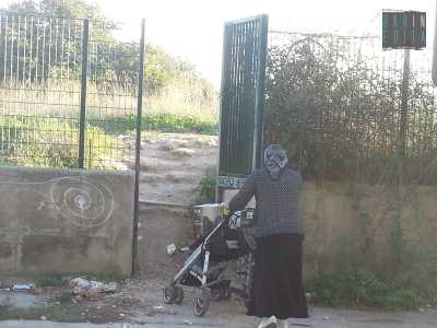 Una donna rom con il suo carico del giorno si accinge ad attraversare il cancello per raggiungere il suo accampamento