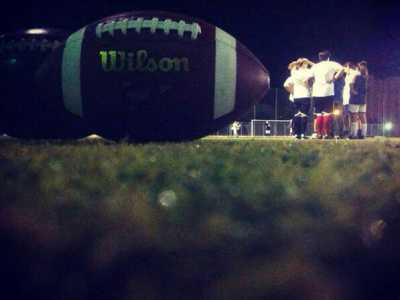 In primo piano, un pallone da football americano. Poco lomtano, le ragazze in cerchio si danno la carica