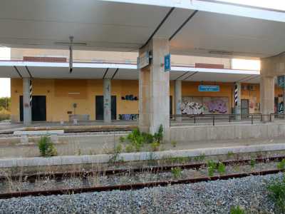 L'interno spettrale della stazione tra vegetazione spontanea, scritte sui muri e il cartello che indica la fermata "Sannicandro di Bari" ancora presente