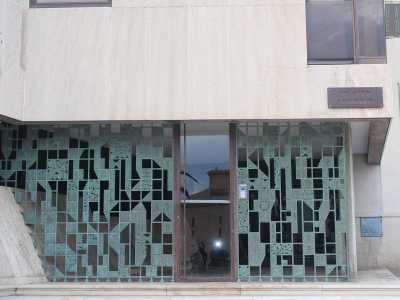 L�edificio presenta al piano terra un ampio spazio vuoto che fa da filtro tra esterno e interno circondato da una cancellata bronzea realizzata dal grande artista pugliese Raffaele Spizzico