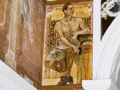 Sulla sinistra � disegnato un fabbro: una baffuta figura maschile a torso nudo, seduta vicino a un�incudine e con in mano un martello. Presenta la scritta labor omnia vincit (�la fatica vince ogni cosa�)