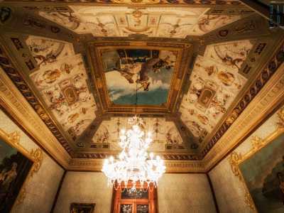 ...dominato da un�alta volta decorata con vari motivi ornamentali �a grottesche�. Le linee geometriche e le svariate figure fanno da contorno al pannello centrale �en plein air�: raffigura una scena dallo stile classico dipinto da Domenico Battista nel 1901