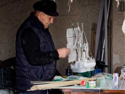 Meuccio, che ha in capo una coppola scura, � all�opera. Lo troviamo appoggiato a un vecchio tavolo...