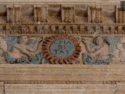 La complessit� della decorazione si infittisce nel fregio, dove foglie intrecciate conducono a uno stemma centrale azzurro acquerellato con la scritta Charitas