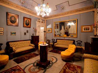 La porta conduce al secondo salottino, quello �blu�. Qui divani e poltroncine ocra, sistemati in cerchio al centro, dominano la scena riflettendosi nello specchio con cornice del medesimo colore...