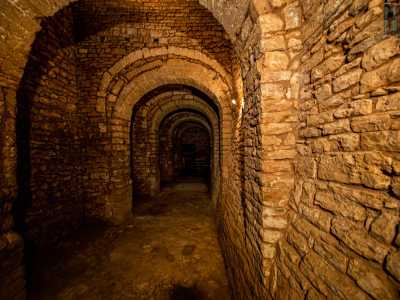 Da una scala in legno risaliamo qualche gradino per accedere a un lungo corridoio, forse un camminamento difensivo del vecchio fortilizio, suddiviso da una serie di spettacolari archi divisi da volte in pietra perfettamente lineari tra di loro