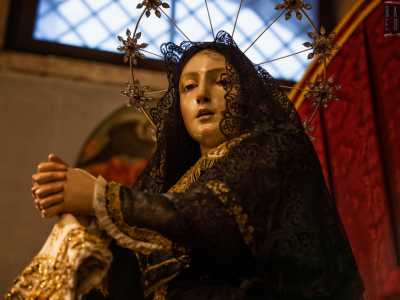 Alla sua sinistra, attorniata da decine di rose e drappeggi rossi, si trova un realistico simulacro di Maria Addolorata...