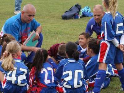 John mentre allena alcune bambine in una scuola calcio. Tra le piccole ci sono anche le sue due figlie