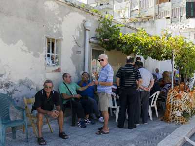 In una stradina laterale un gruppo di anziani cerca di svagarsi all'ombra di una rampicante