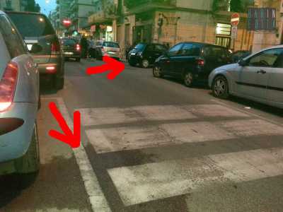 L'acqua sull'asfalto (freccia in basso) e l'auto ferma sull'incrocio di una stradina chiusa (freccia a destra)