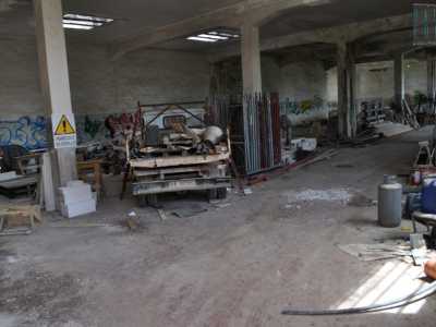 Ci sporgiamo per scrutarne l�interno. Qui regna solo il disordine, con un camion pieno di attrezzi da muratore e poi parti di un�impalcatura, sacche di cemento, mattoni e bombole, tubi e altri oggetti da lavoro. Su una colonna spicca un cartello bianco e giallo con una scritta nera: �Pericolo di crollo�. Il tutto sovrastato da un soffitto annerito e corroso dalla muffa. Le pareti si presentano piene di disegni e scritte